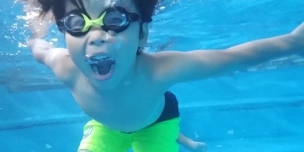 Child swimming underwater with goggles open mouth.