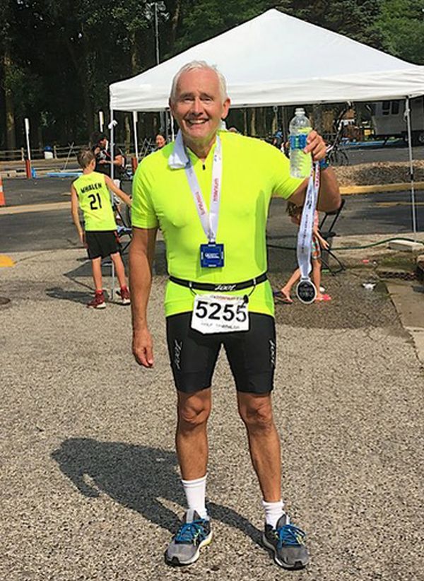 happy man in a green neon shirt, and black shorts, at the end of a race holding a medal