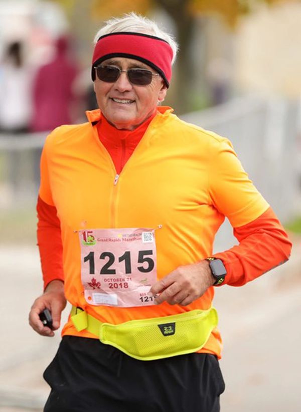 happy man running a race in black shorts, red headband, orange and yellow shirt