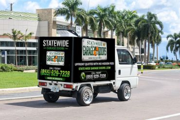 Small truck with a garage door business advertisement driving on a sunny street.