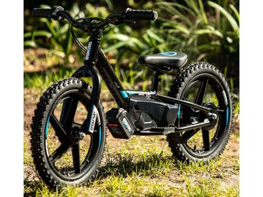 Black and blue electric kids bike with rugged tires on grass.