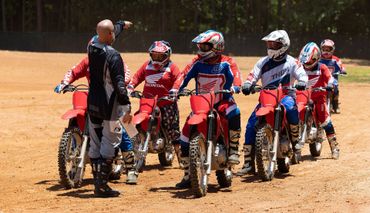 Instructor guides motocross riders during training on dirt track.