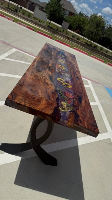 Wooden table with embedded colorful flowers and unique black metal base.