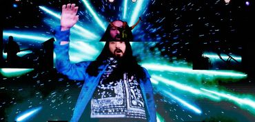 DJ and electronic music producer Steve Aoki plays on a stage with a giant image of himself.
