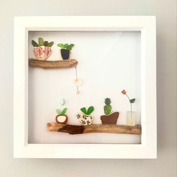 Framed art with small plant pots and green leaves on wooden shelves.