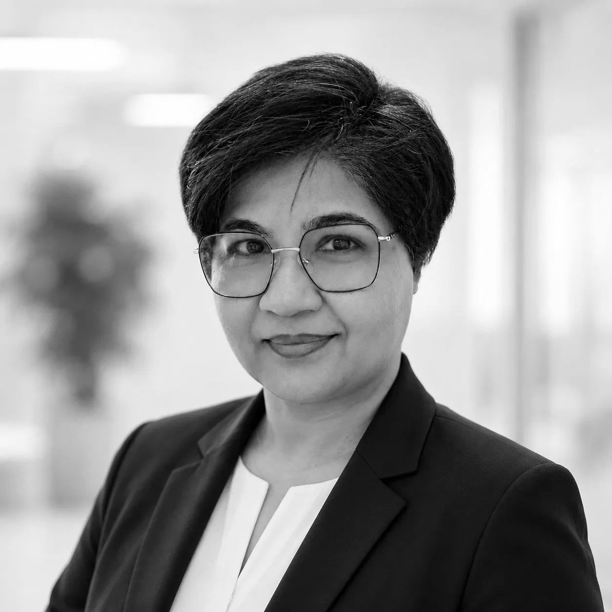 Professional woman with glasses in a business suit smiles confidently.