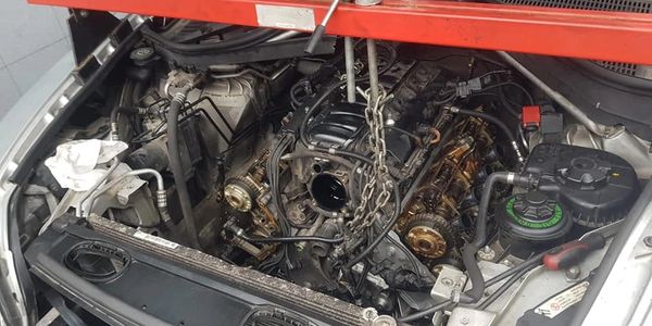 Car engine undergoing repair with parts removed and a chain hoist attached.