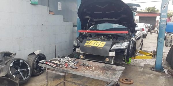 A car on a lift in a garage with tools and parts scattered around.