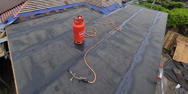 Roof repair with a gas cylinder and torch on a flat roof.