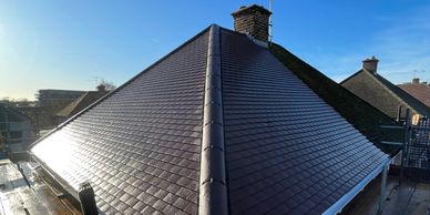 Shiny, newly installed roof tiles on a house under clear blue sky.