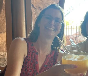 Smiling woman with glasses holding a large orange beverage in a cozy indoor setting.
