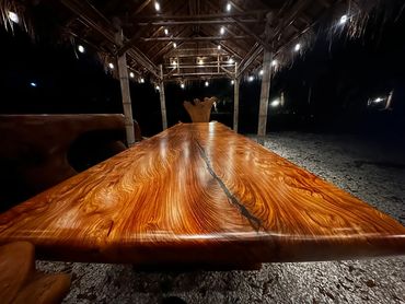 A stunning 15 ft live-edge dining table featured at night under a custom tiki hut by Decor Direct,