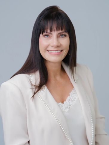 Smiling woman in white blazer with lace top.