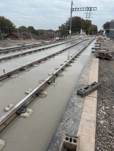 Newly laid railway tracks set in fresh concrete under overcast sky.
