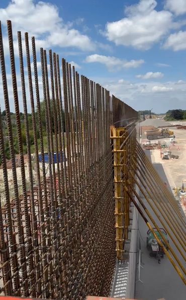 Tall reinforced steel bars set up for a large concrete wall construction under a blue sky.