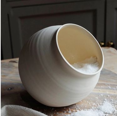 A ceramic salt cellar tipped over with salt spilled on a wooden surface.