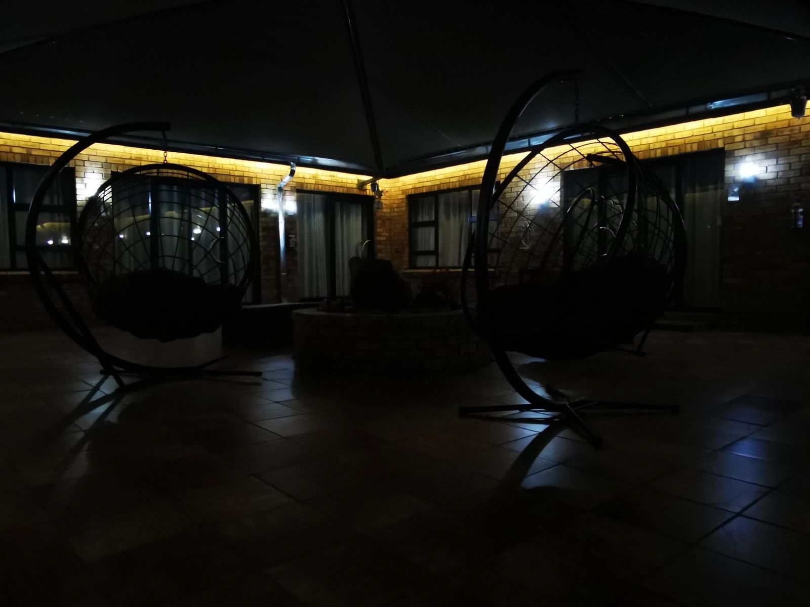 Dimly lit outdoor patio with hanging egg chairs under a canopy at night.