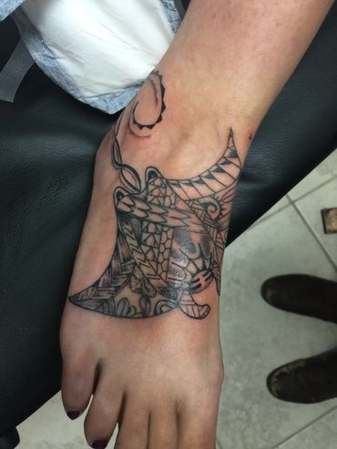 Intricate black dragon tattoo on foot with geometric patterns.