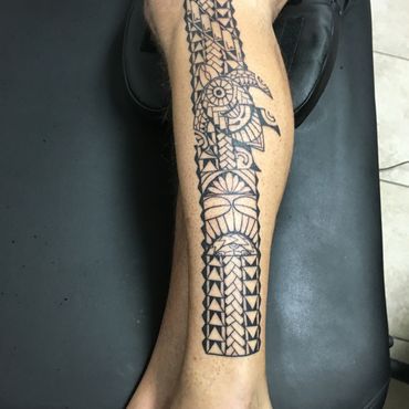 Intricate black tribal tattoo on leg with geometric patterns.