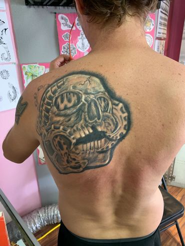 Large skull tattoo on upper back with mechanical elements.