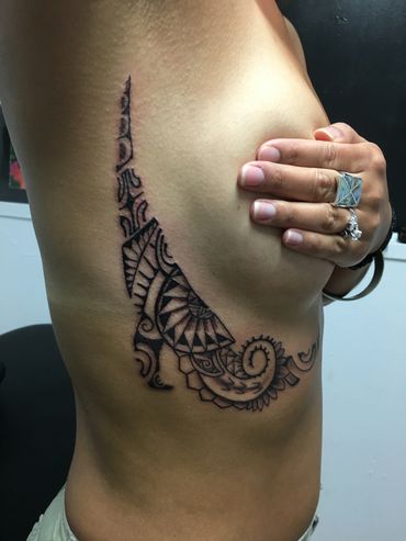 Decorative tribal tattoo on side torso with hand covering the chest.