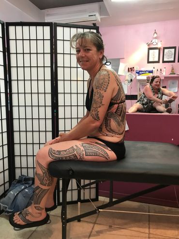 Tattooed woman sitting on a massage table smiling.
