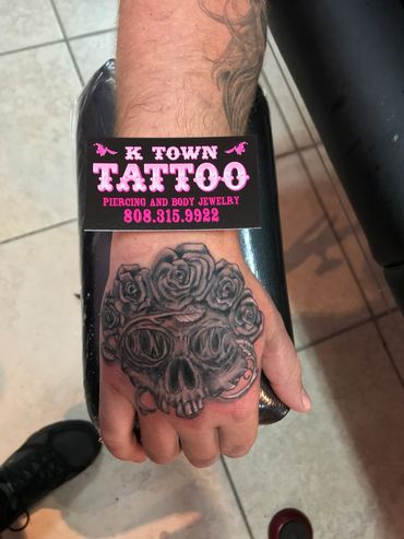 Hand tattoo of a skull with roses and a business card.