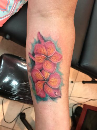Tattoo of orange and pink flowers with green background on forearm.