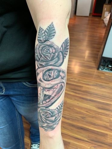 Black and grey tattoo of roses and skull on forearm.