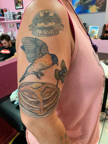 Arm tattoo with Batman logo, bird, walnut, and leaves.