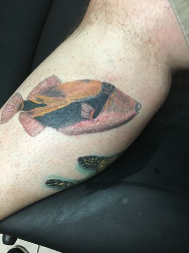 Tattoo of a colorful fish on a leg.