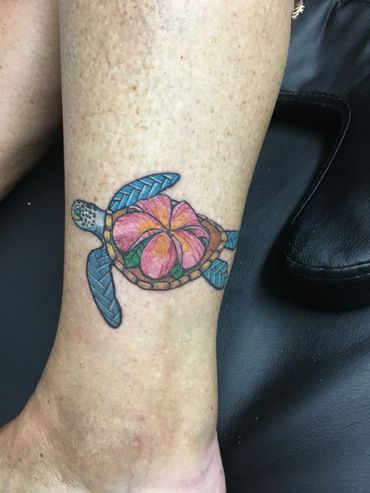 Colorful sea turtle tattoo with a pink flower on a leg.