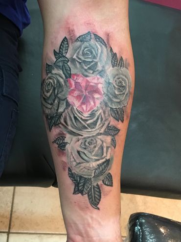 Forearm tattoo of gray roses surrounding a pink diamond heart.
