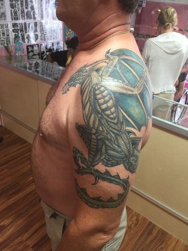Detailed dragon tattoo on a man's upper arm and shoulder.