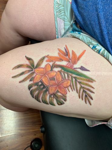 Floral tattoo on thigh with tropical flowers and leaves.