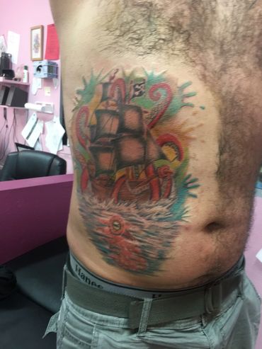 Colorful tattoo of a ship and sea creatures on a man's side torso.