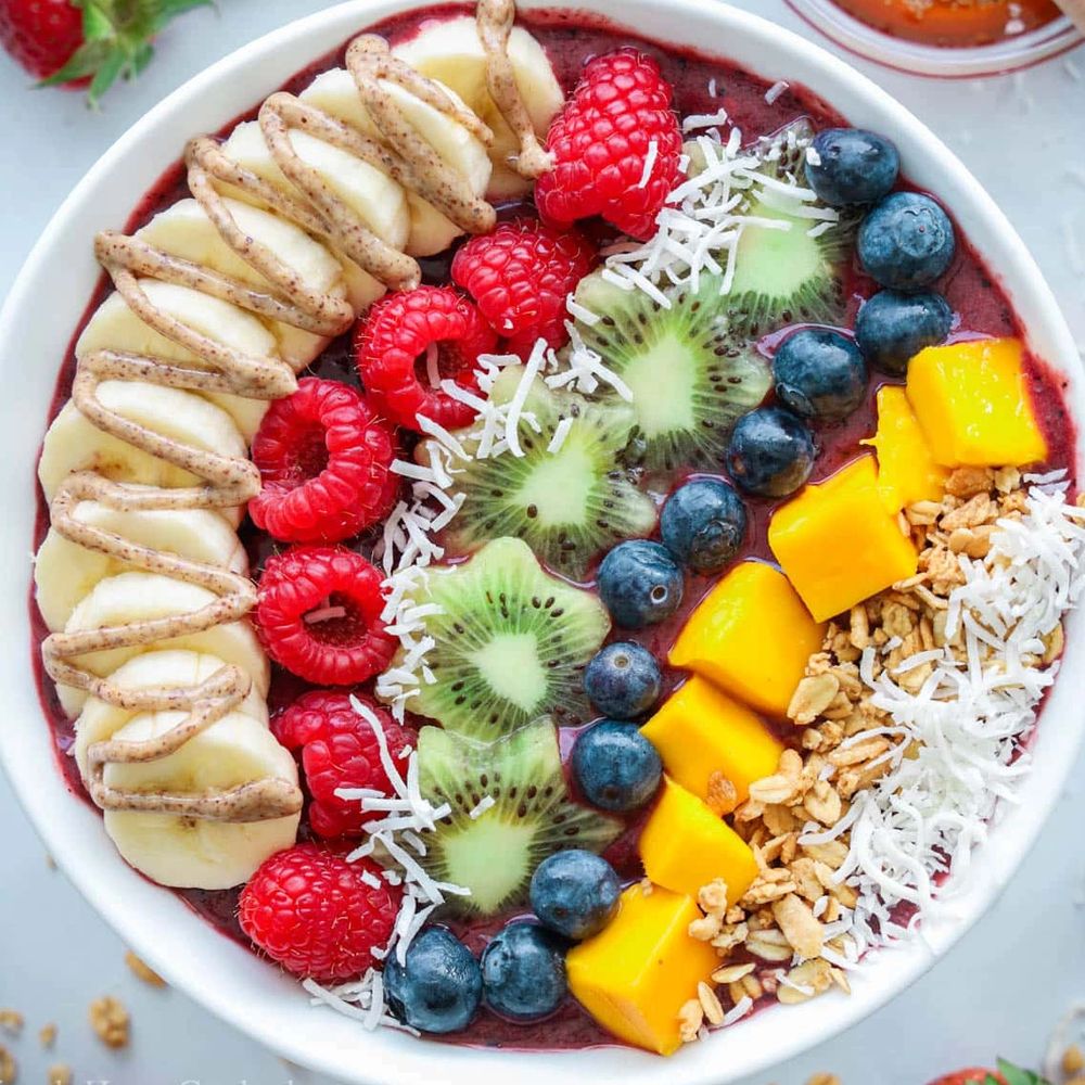 colorful acai bowl topped with banana, raspberry, kiwi, blueberry, mango, coconut and peanut butter