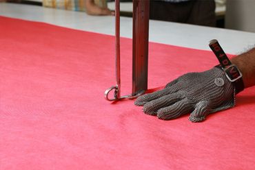 Person cutting fabric with a protective glove on hand.