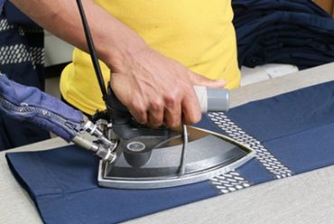 A person ironing a pair of blue pants with a professional iron.
