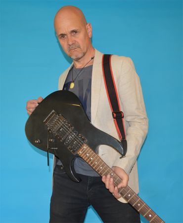 Mito Mora de pie con una guitarra eléctrica negra colgada de los hombros