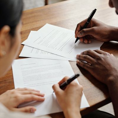 Two people signing documents together at a wooden table.