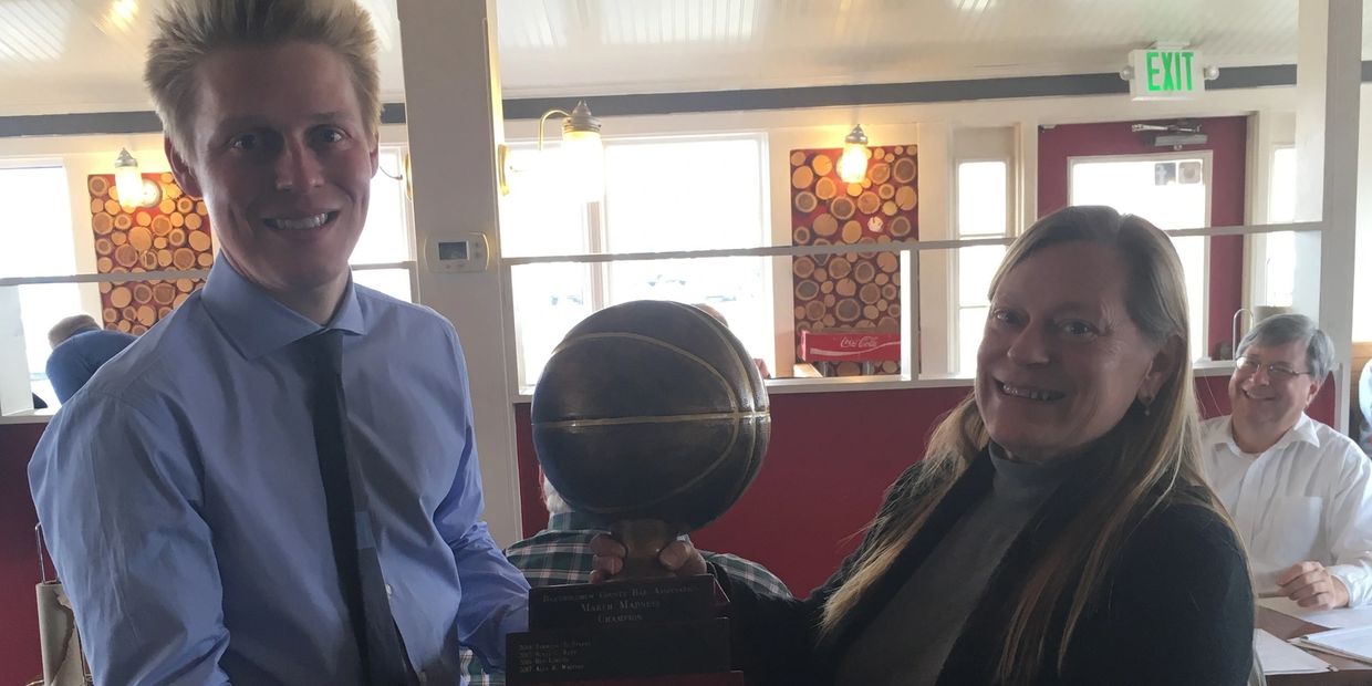 A man in a blue shirt and a woman in a turtle neck hold a march madness trophy from BCBA event