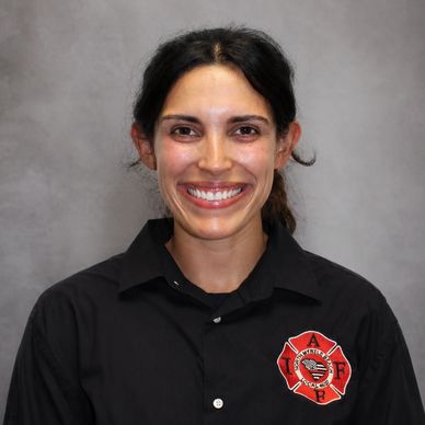 Smiling woman in a black firefighter uniform with a badge.