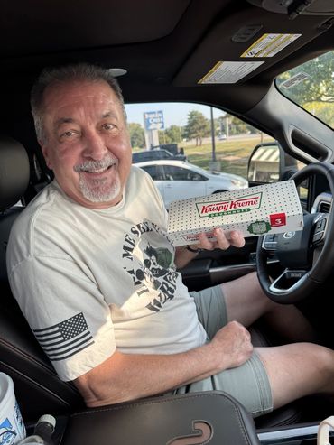 Smiling man holding a Krispy Kreme box inside a car.