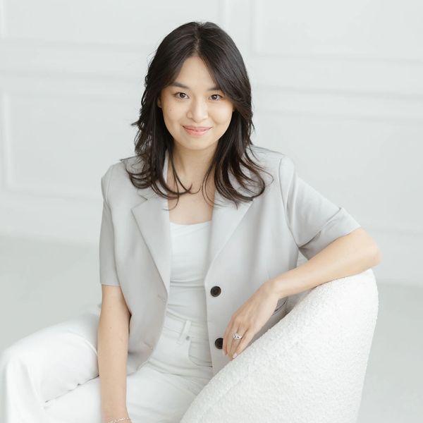 Young woman in light gray blazer and white pants smiling.
