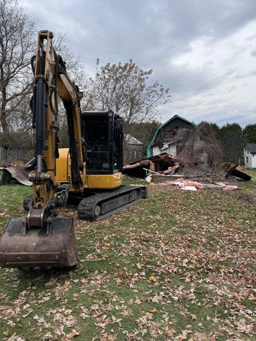 An excavator sitting in front of a shed mid-demolition.
