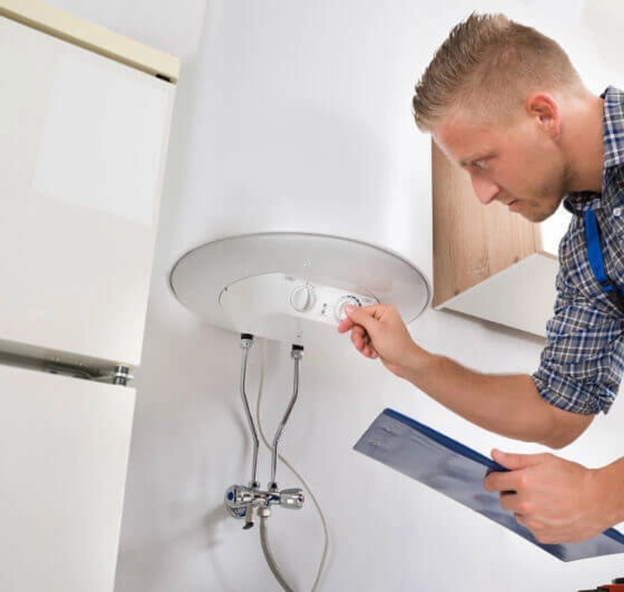 Technician adjusting a water heater thermostat with clipboard in hand.