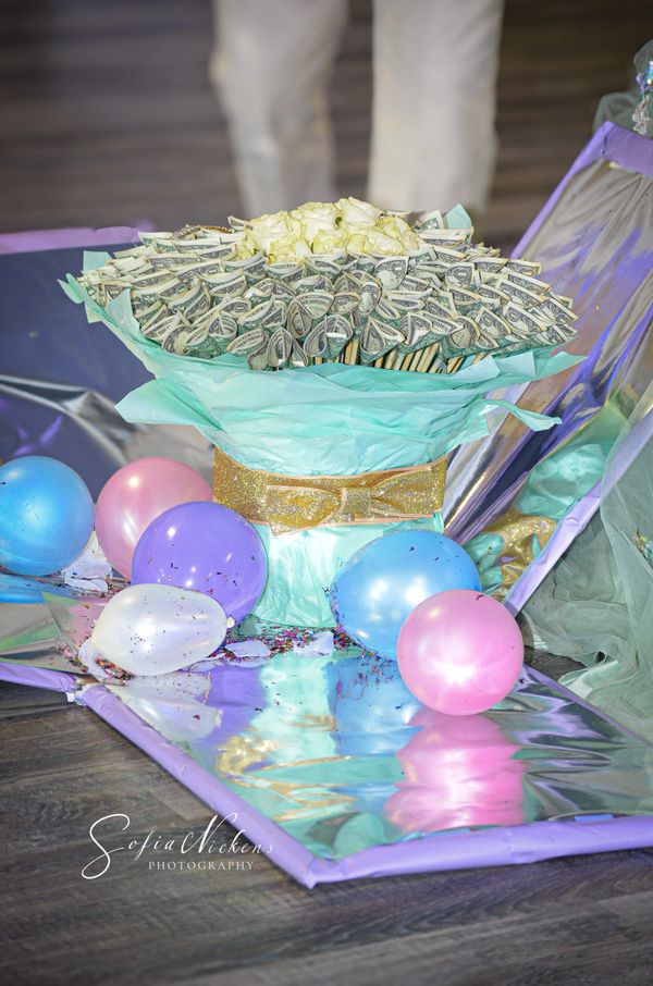 Creative bouquet made of dollar bills and white roses with colorful balloons around.