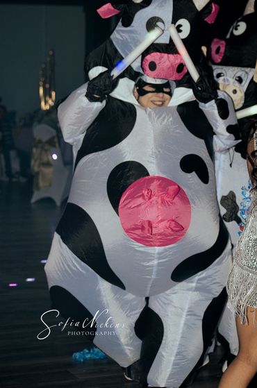 People dressed in inflatable cow costumes dancing with glow sticks at a party.