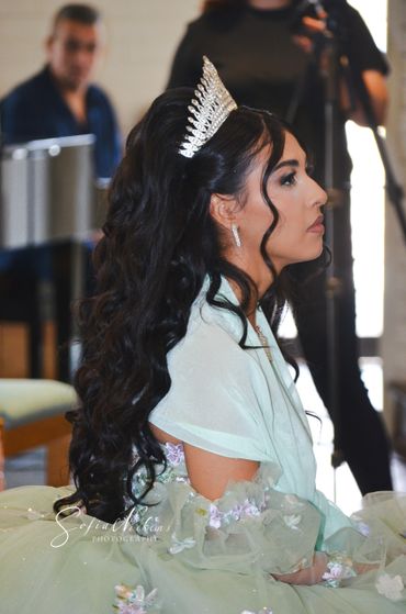Young woman in a tiara and elegant dress sits in profile.